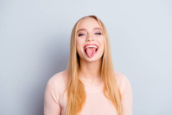 Close up portrait of funny childish playful careless carefree cheerful excited joyful beautiful delightful with long blond straight hairdo woman demonstrating tongue isolated on gray background
